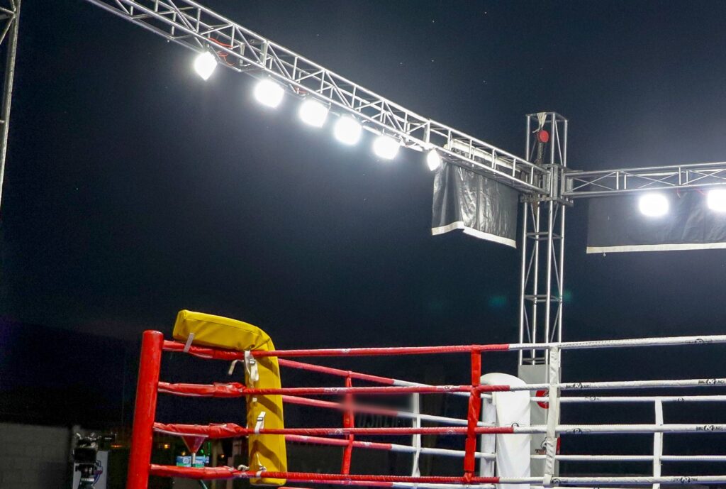 Empty boxing ring under bright truss lights at night